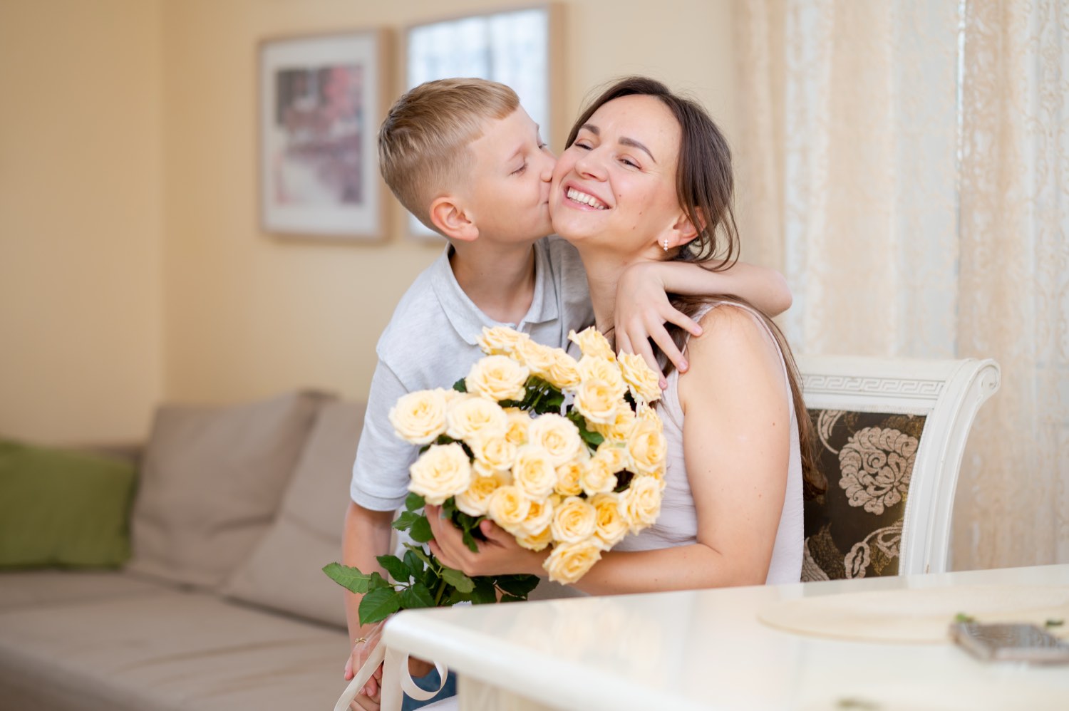 A young boy kissing his smiling mother, who is holding a bouquet of roses